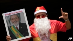 ARCHIVO - Un partidario del presidente brasileño Luiz Inácio Lula da Silva vestido de Papá Noel señala la letra "L" de Lula, con una foto que dice en portugués "¡Salud Presidente!", durante una reunión de apoyo al líder en Brasilia, Brasil, el 10 de diciembre de 2024.