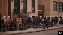 ARCHIVO - Migrantes hacen cola en el frío mientras buscan un refugio fuera de un centro de asistencia a migrantes en la escuela primaria St. Brigid, el 5 de diciembre de 2023, en Nueva York.
