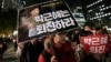 FILE - A South Korean protester carries a placard showing images of South Korean President Park Geun-hye and Choi Soon-sil, top left, during a rally calling for Park to step down, Nov. 2, 2016.