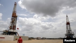 ARCHIVO - Un trabajador petrolero camina junto a plataformas de perforación en un pozo operado por la petrolera estatal venezolana PDVSA, en la faja petrolera del Orinoco, rica en petróleo, el 16 de abril de 2015.