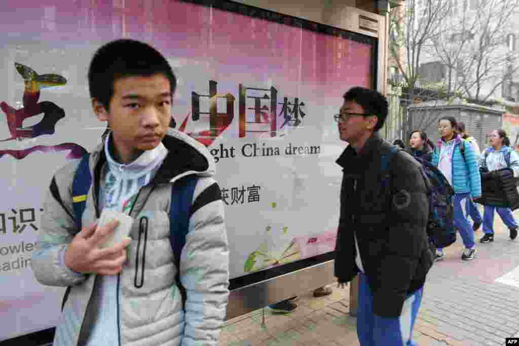 2018年3月12日，北京一所学校外面，少年人走过宣传牌，牌上写着中英文口号&ldquo;点亮中国梦 知识改变命运 付出收获财富&rdquo;。