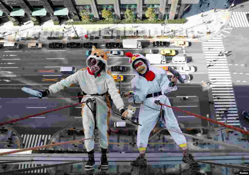Window cleaners, dressed as a rooster, this year&#39;s Chinese zodiac animal and a dog, next year&#39;s Chinese zodiac animal, pose for photographers as they clean the windows of Ryumeikan hotel during a promotional event to celebrate the upcoming new year in Tokyo.