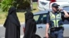 Two women stand next to a policeman blocking a road where police officers are searching a house in the Melbourne suburb of Meadow Heights, Australia, Dec. 23, 2016.