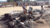 FILE - People stand amid the damage at a camp for displaced people after an attack by suspected members of the Islamist Boko Haram insurgency in Dalori, Nigeria, Nov. 1, 2018. 