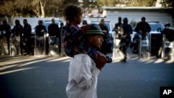 Un migrante carga a un niño frente a policías mexicanos afuera de la Unidad Deportiva Benito Juárez en Tijuana, México.