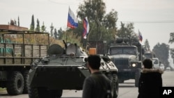 ARCHIVO - Combatientes sirios observan vehículos blindados rusos pasar cerca de la base aérea de Hmeimim, una base aérea siria actualmente operada por Rusia, en la ciudad de Hmeimim, al sureste de Latakia, Siria, el lunes 16 de diciembre de 2024. AP