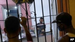 Un hombre hace "arepas" con el carrito de comida La Flaca instalado en la vivienda de la propietaria, mientras clientes esperan al otro lado de las barras en el barrio de Santa Rosalía en Caracas, Venezuela. Agosto 23, 2020.