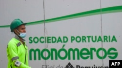 ARCHIVO - Un trabajador camina frente a un letrero de Monómeros en Barranquilla, Colombia, en octubre de 2021.