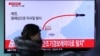 A woman at a train station in Seoul walks by a TV screen showing a news report about North Korea's missile test, March 6, 2017.