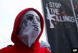 A masked protester stands next to a banner condemning President Rodrigo Duterte's war on drugs, during a rally to coincide with his third State of the Nation Address, July 23, 2018, in Quezon city, metropolitan Manila, Philippines.