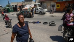 ARCHIVO - Una mujer camina junto al cuerpo de un hombre, que yace a mitad de una calle de Puerto Príncipe, el jueves 20 de abril de 2023. 