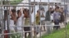 FILE - Asylum-seekers look through a fence at the Manus Island detention center in Papua New Guinea, March 21, 2014. 