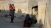 FILE - An internally displaced woman sits outside a tent in Idlib province, Syria, July 30, 2018, as another woman with child looks on. 