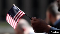 Seseorang memegang bendera AS selama upacara naturalisasi Kewarganegaraan dan Imigrasi AS (USCIS) di Rockefeller Plaza di New York City, AS, 17 September 2019. (Foto: Reuters/Shannon Stapleton)