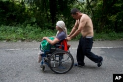 El migrante hondureño Omar Orella empuja a su compañera Nery Maldonado Tejeda en una silla de ruedas, mientras viajan con cientos de otros hondureños que se dirigen a EE.UU., cerca de Chiquimula, Guatemala, el martes 16 de octubre de 2018.