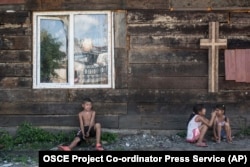 UKRAINE -- Roma children rest in the shade of a church wall inside a Roma encampment on the outskirts of Uzhhorod, June 4, 2018