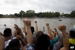 Migrantes hondureños cantan su himno nacional en la orilla del río Suchiate, en la frontera entre Guatemala y México, en Tecún Umán, Guatemala, el 18 de octubre de 2018.