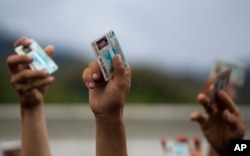 Los migrantes hondureños levantan sus tarjetas de identificación nacionales cuando la policía guatemalteca los bloquea, después de que su caravana cruzó la frontera Honduras-Guatemala sin incidentes, en Esquipulas, Guatemala, el lunes 15 de octubre de 2018.