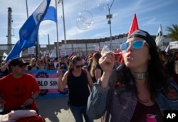 Una mujer sopla burbujas durante una marcha en apoyo de la caravana de migrantes cerca de la frontera de EE. UU. y México, el domingo 25 de noviembre de 2018, en San Diego