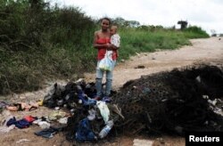 La venezolana Joanna y su hijo Bruno, del estado Anzoátegui, posan junto a sus pertenencias y colchones quemados por civiles mientras sostiene pañales donados en el control fronterizo de Pacaraima, estado de Roraima, Brasil, el 19 de agosto de 2018.