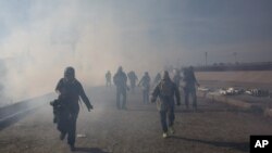 Migrantes corren del gas lacrimógeno lanzado por agentes estadounidenses, entre fotoperiodistas que cubren la frontera entre México y Estados Unidos, después de que un grupo de migrantes lograra pasar a las autoridades mexicanas en el cruce de Chaparral en Tijuana, México.