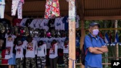 Un hombre espera un autobús de transporte público junto a un puesto que vende camisetas, banderas y gorras, con alusiones al sandinismo, en una parada de autobús en Managua, Nicaragua, el miércoles 3 de noviembre de 2021. (Foto AP/Andrés Núñez)