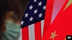 资料照：一名戴口罩妇女坐在显示美中国旗的屏幕前