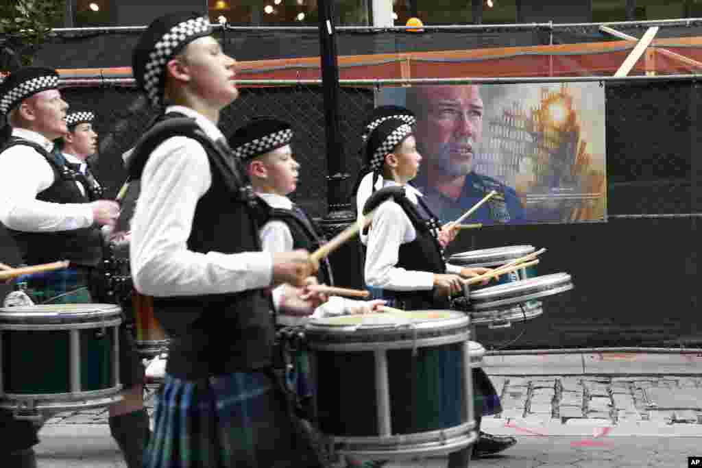 Barisan drumband melewati karya seni yang menggambarkan petugas kepolisian Kota New York yang gugur saat peristiwa 11 September 2001, ketika mereka berbaris selama peringatan prosesi NYPD Emerald Society Pipes & Drums di kota New York.