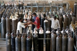 Personas cargan cilindros de oxígeno después de rellenarlos en una fábrica, en medio de la propagación de la enfermedad del coronavirus (COVID-19) en Ahmedabad, India, el 25 de abril de 2021.