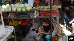 Una vendedora venezolana hace manicura a otra mujer mientras espera por clientes en el mercado de Las Pulgas, en Maracaibo, el 29 de diciembre de 2023.