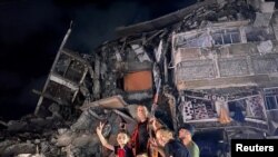 Grupo de personas gesticula cerca de los escombros de un edificio dañado mientras los palestinos celebran en las calles tras un alto el fuego, en la ciudad de Gaza el 21 de mayo de 2021.