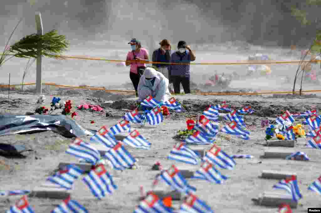 Un trabajador del Cementerio de la Bermeja en San Salvador, El Salvador, pone flores en la tumba de una persona que falleci&#243; de COVID-19.