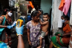 A healthcare worker checks the temperature of residents of a slum area using an electronic thermometer, in Mumbai, India, July 6, 2020.