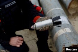 ARCHIVO- El militar ucraniano Igor Ovcharruck sostiene una bomba de racimo desactivada de un misil MSLR, entre una exhibición de piezas de cohetes utilizados por el ejército ruso, que un experto en municiones ucraniano dijo que no explotaron en el impacto, en la región de Kharkiv, Ucrania, el 21 de octubre de 2022.