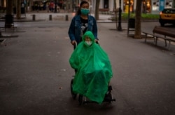Un hombre que usa una máscara facial y una capa para cubrir la lluvia es trasladado en una silla de ruedas a lo largo de un bulevar en Barcelona, España, el miércoles 9 de septiembre de 2020.