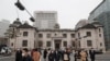 People wearing face masks walk by the headquarters of the Bank of Korea in Seoul, South Korea, March 4, 2021. South Korea's central bank says the country's economy shrank for the first time in 22 years in 2020. 