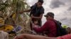 Una niña migrante venezolana es asistida por compatriotas mientras intentan pasar entre alambres de púas colocados a lo largo de las orillas del río Grande, en Eagle Pass, EEUU, el 6 de octubre de 2023.