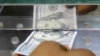 Foto de ilustración, un hombre inserta un billete de cien dólares en una ventana de un cambio de moneda local. Fotografía tomada el 29 de junio de 2021.