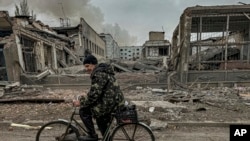 FILE - Seorang pria mengendarai sepeda di depan kantor pos yang hancur akibat serangan udara Rusia di Kurakhove, wilayah Donetsk, Ukraina, 7 November 2024.