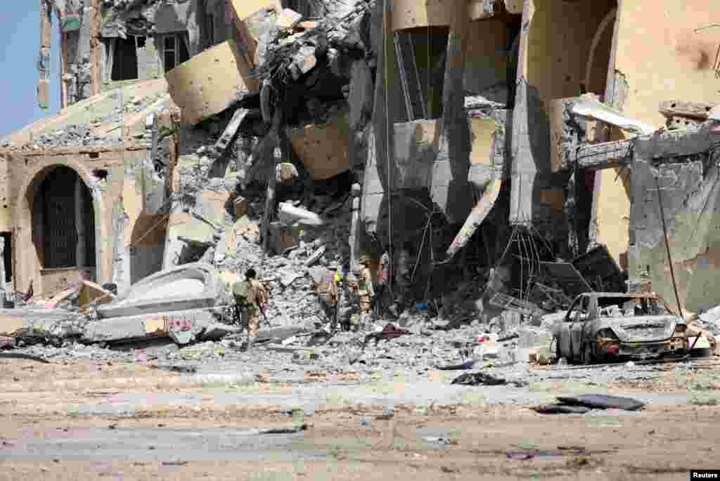 Pasukan Libya yang didukung PBB melewati reruntuhan bangunan dalam perang melawan militan ISIS di Sirte, Libya.