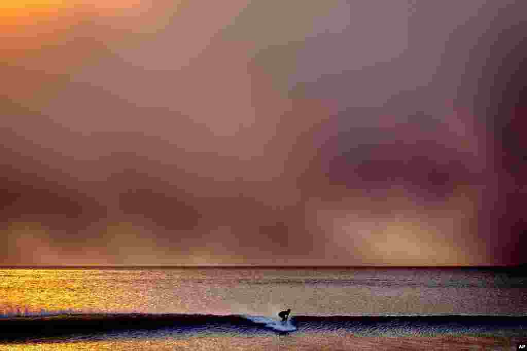 Un surfista se desplaza sobre una ola en Santa Mónica, California, durante el atardecer bajo un cielo ennegrecido por el incendio de Palisades en Pacific Palisades, el 7 de enero de 2025.