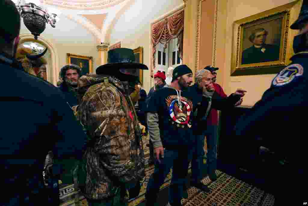 Manifestantes caminan mientras los oficiales de la polic&#237;a del Capitolio observan en un pasillo cerca de la c&#225;mara del Senado en el Capitolio en Washington.