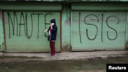 FILE - A person is seen using a mobile phone while passing a shuttered store front with "MAUTE-ISIS" graffiti, in Marawi city, southern Philippines, Oct. 20, 2017.